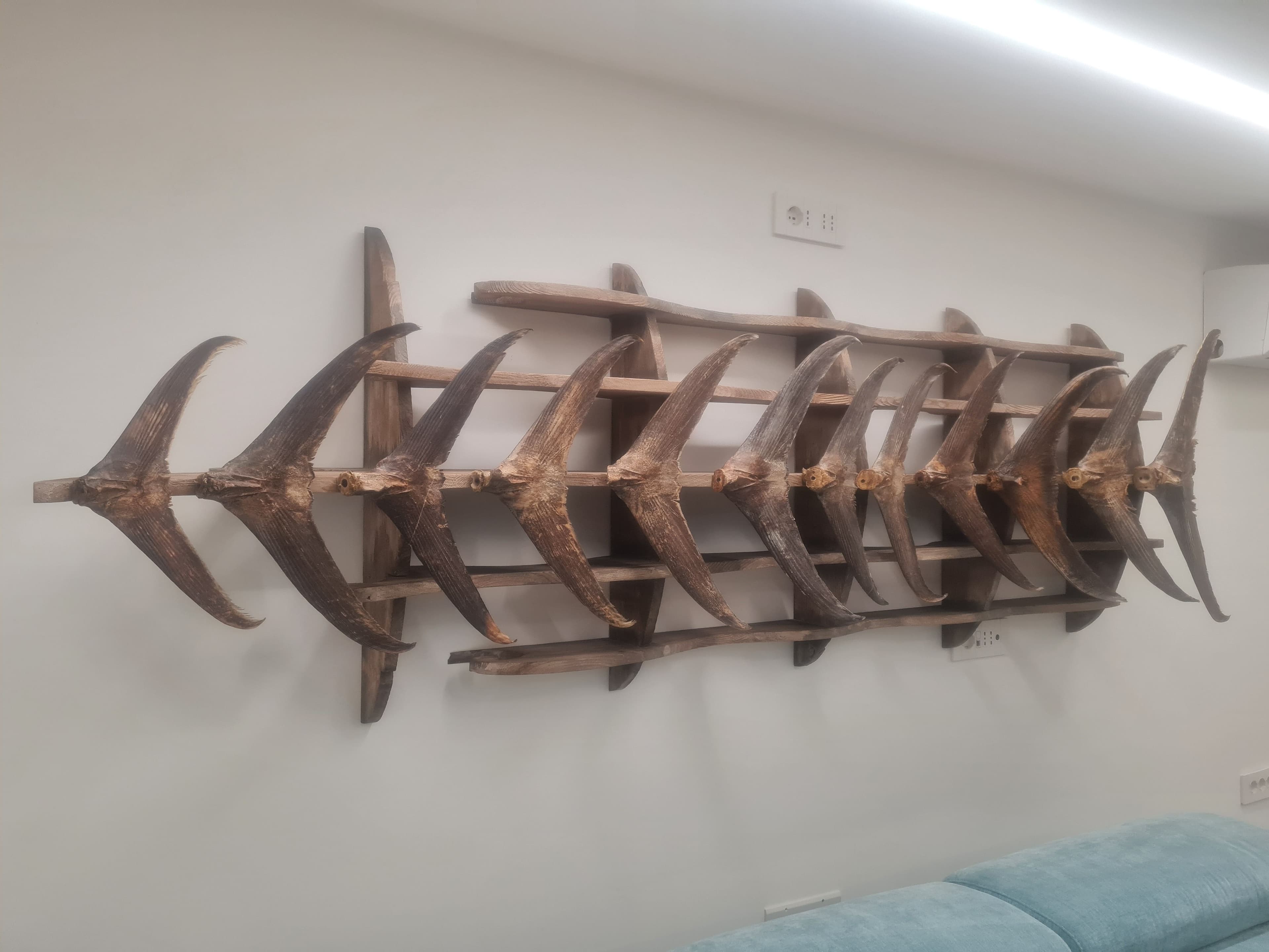 Primo piano dell'opera d'arte a parete composta da code di pesce su struttura in legno a forma di chiglia di barca e onde.
