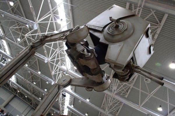 Inquadratura dal basso dell'AT-ST completato e installato sotto il soffitto a traliccio del padiglione fieristico.