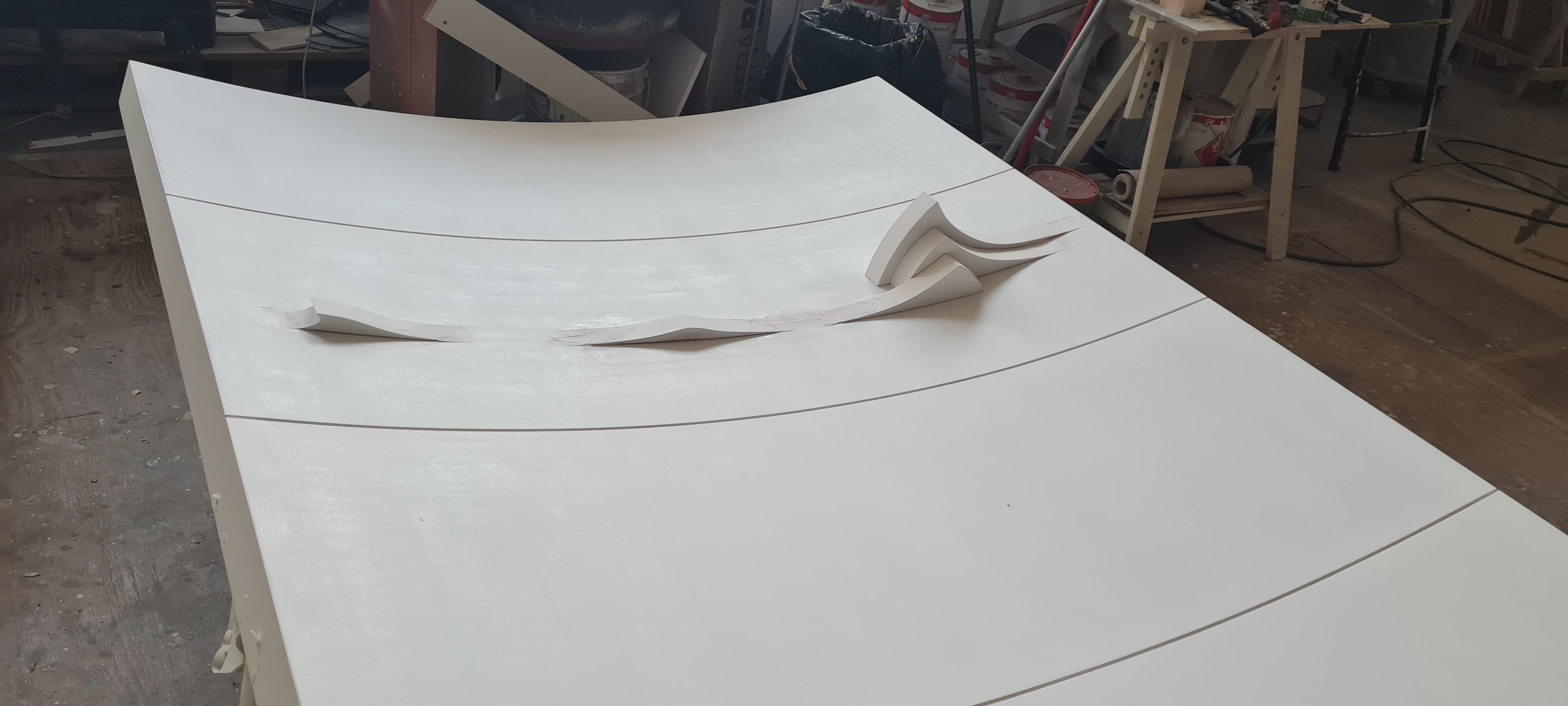 Pannello di legno curvo bianco poggiato su sostegni durante la fase di preparazione superficiale.