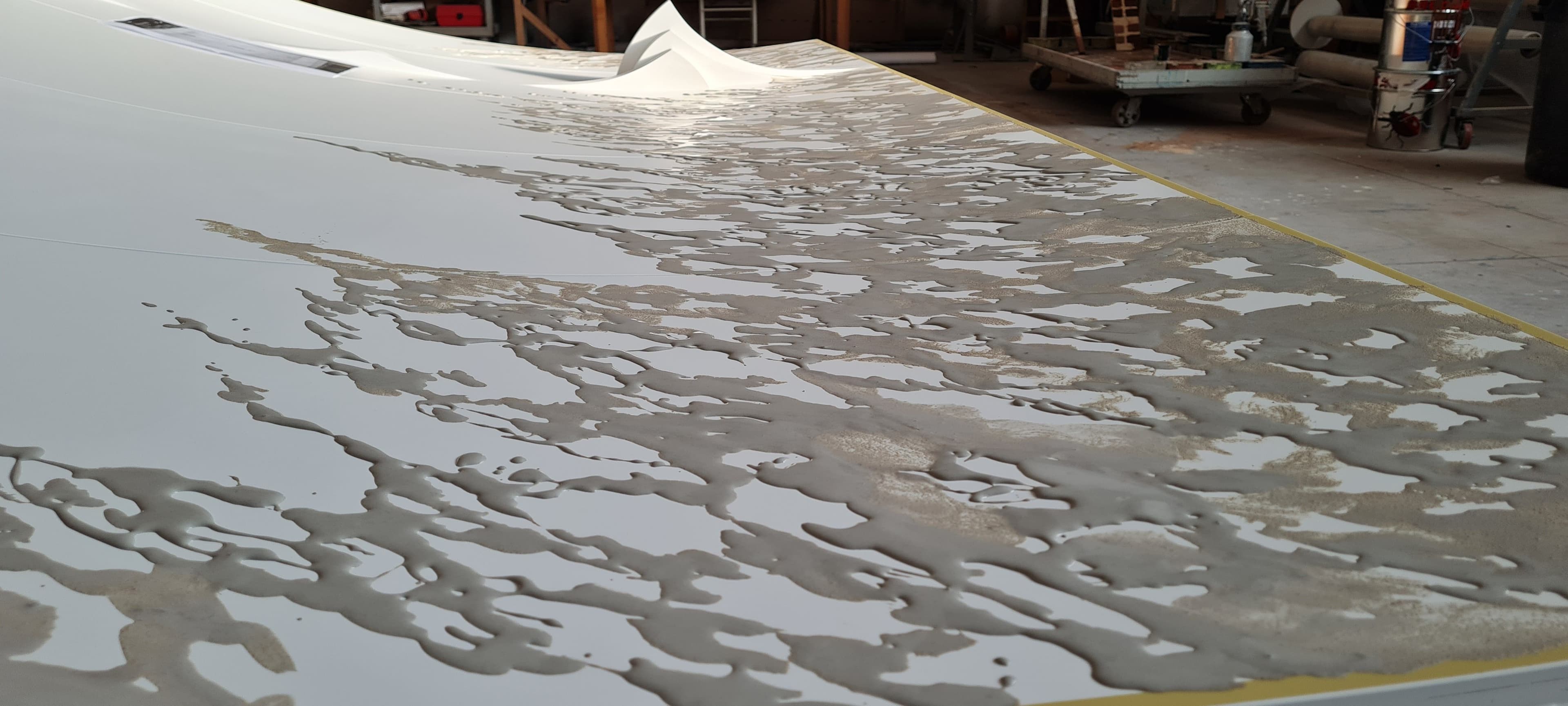 Applicazione di stucco materico dorato e grigio su superficie bianca per creare una texture irregolare.