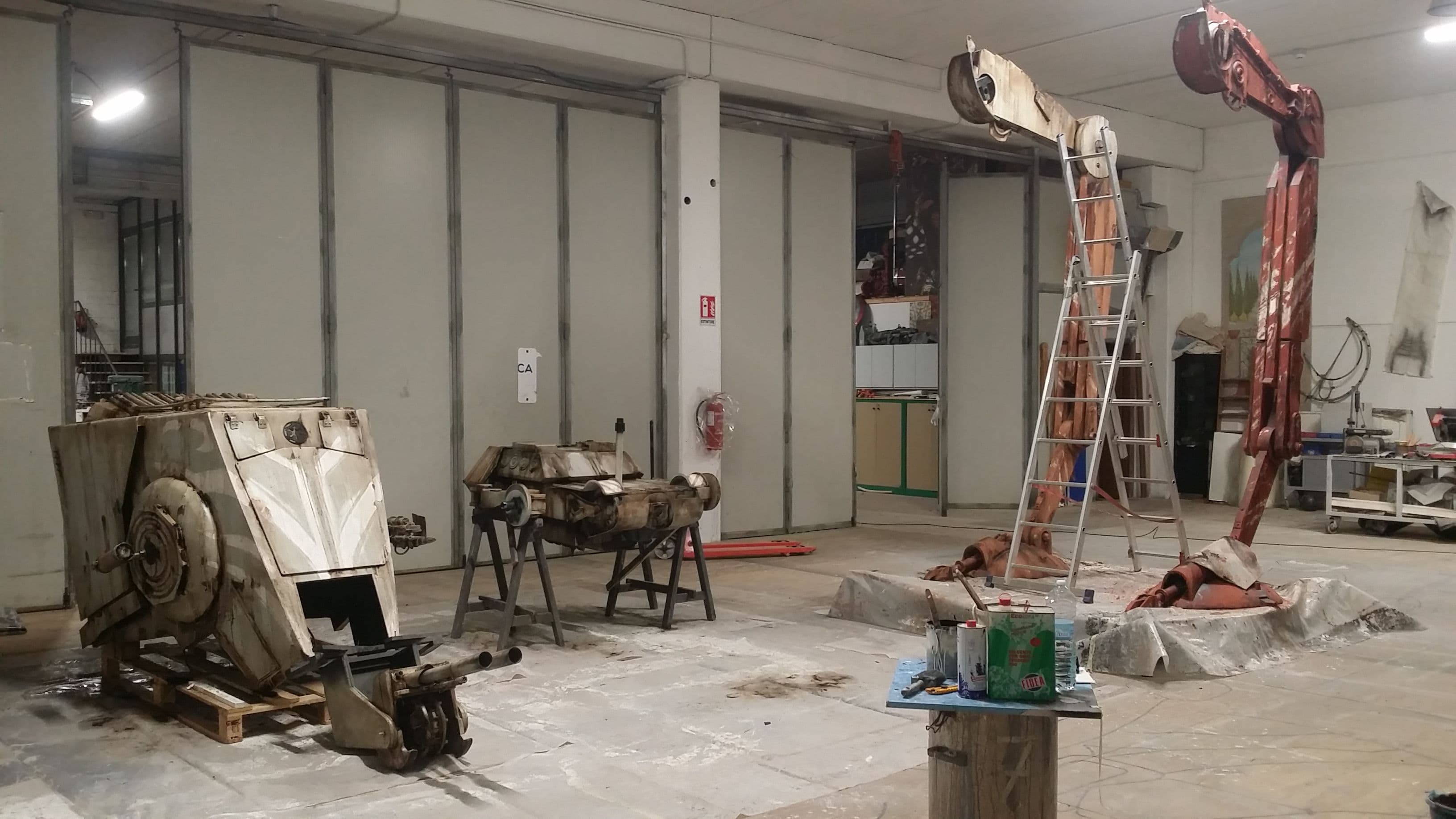 Vista panoramica del laboratorio scenografico con i vari elementi dell'AT-ST (testa, corpo e gambe) disposti nello spazio di lavoro.